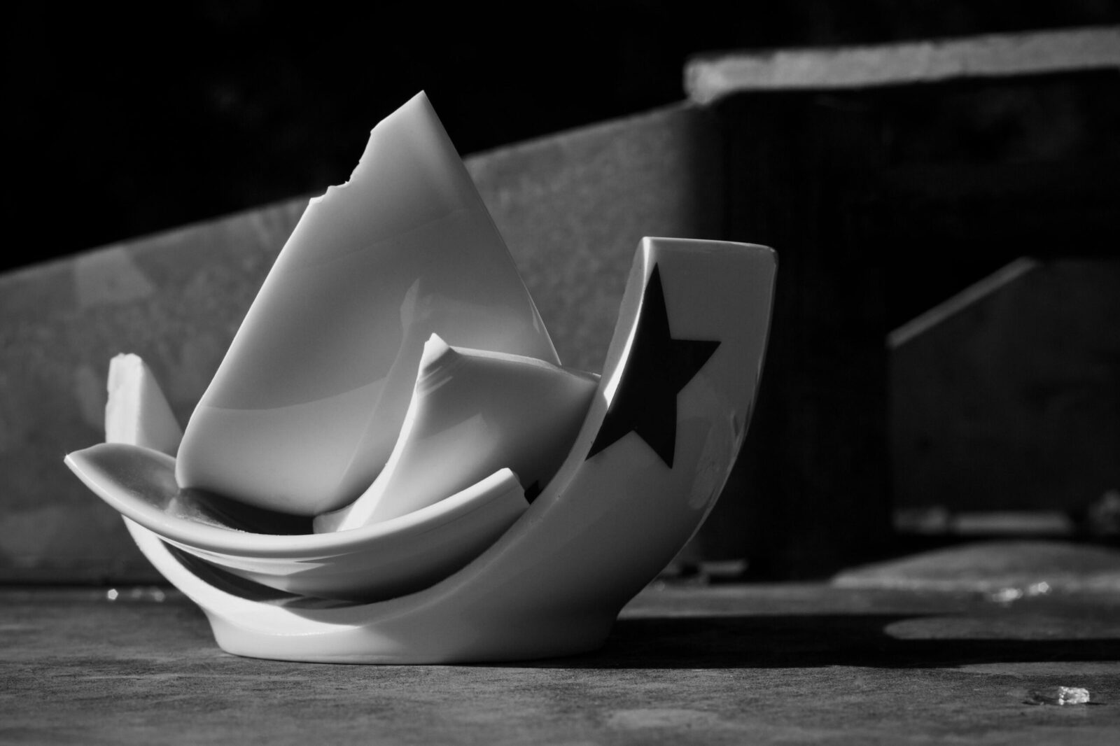 A black and white artistic photo of a broken ceramic bowl with a star design.